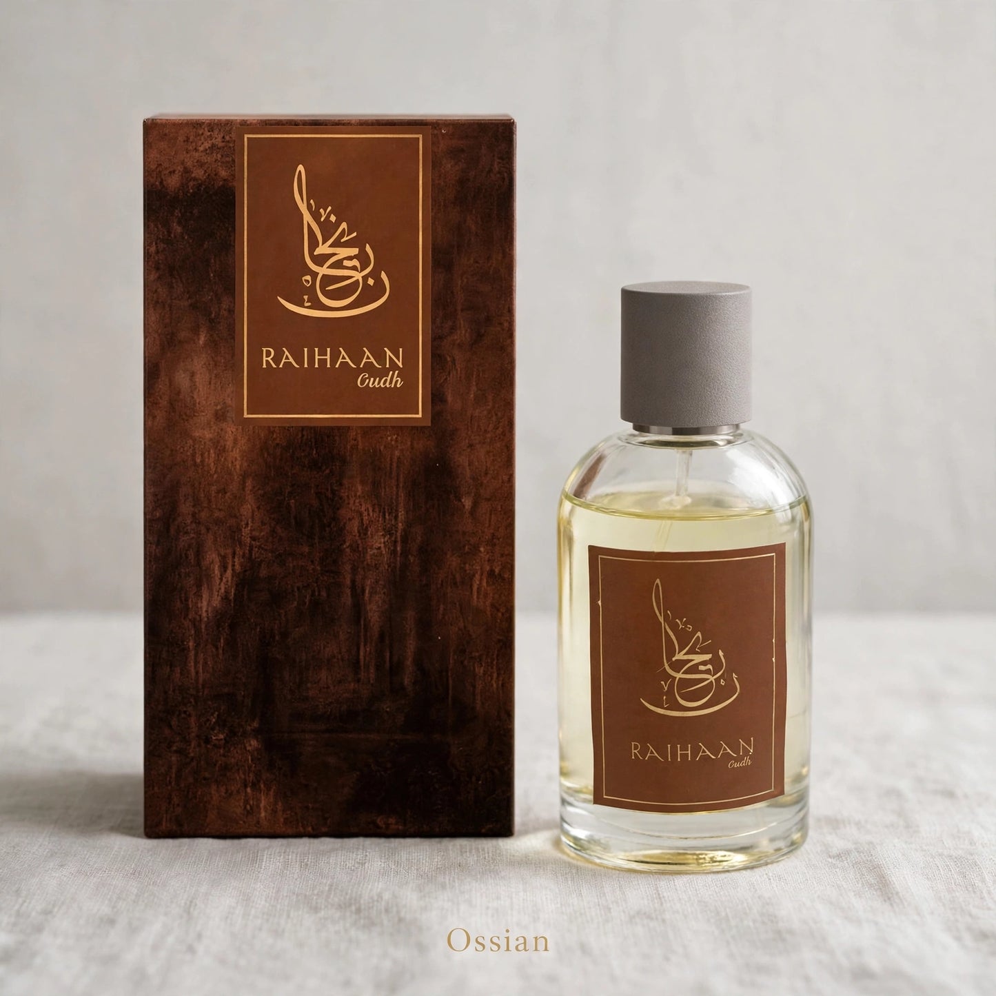 A clear glass perfume bottle with a gray cap stands beside a tall dark brown textured box. Both pieces feature a brown label with a gold coffee cup logo and the brand name RAIHAAN Ouds.