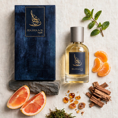 A bottle of Raihaan Scents fragrance with a dark blue box, styled with citrus slices, cinnamon sticks, amber crystals, and green leaves on a light textured background.