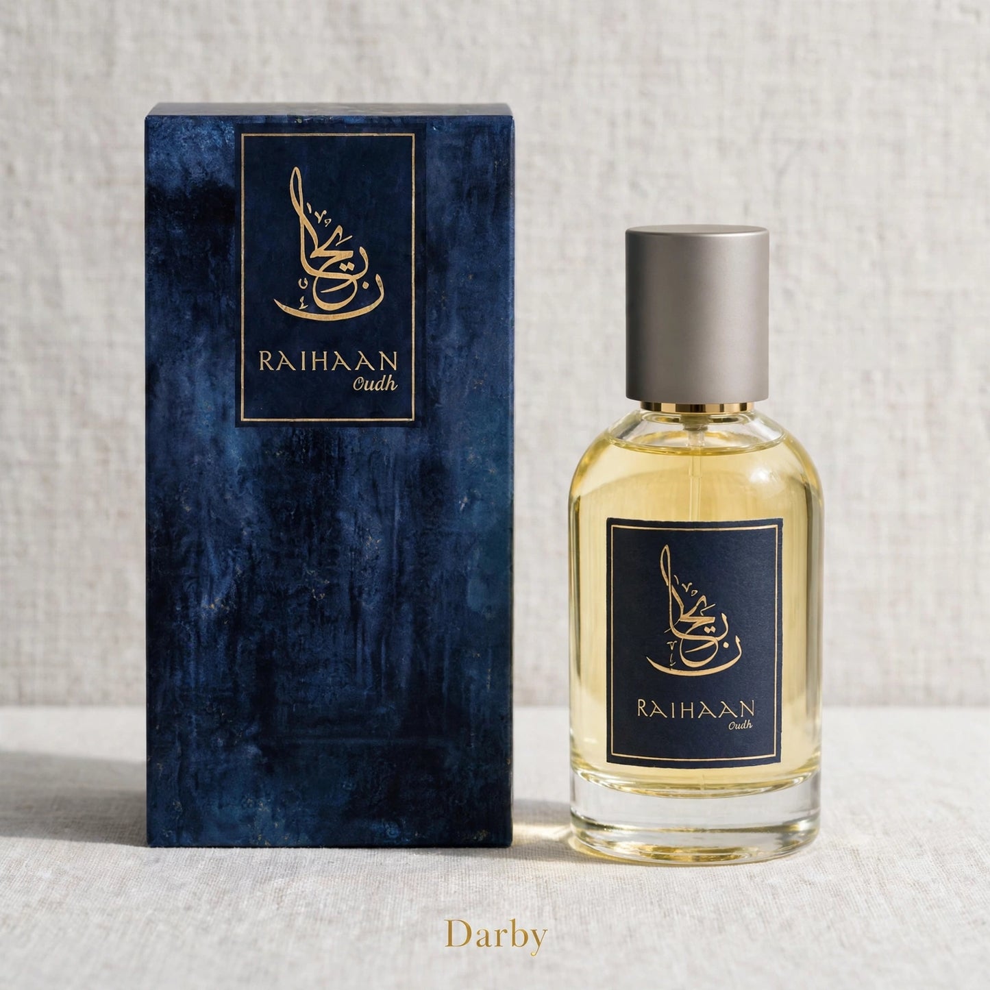 A bottle of Raihaan Darby perfume with a textured dark blue box, shown on a light textured background. The bottle is made of clear glass containing a light golden-yellow liquid, has a metallic silver cap, and a dark blue label with gold Arabic calligraphy and the brand name 'RAIHAAN'.