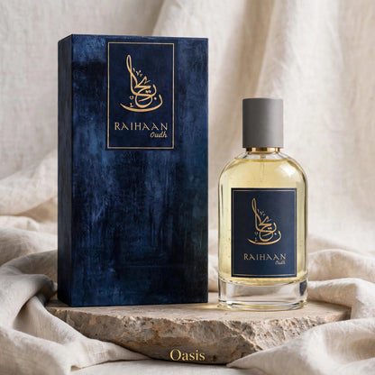 A bottle of Raihaan Oasis perfume next to its dark blue textured box, styled on a stone slab with draped beige fabric in the background.