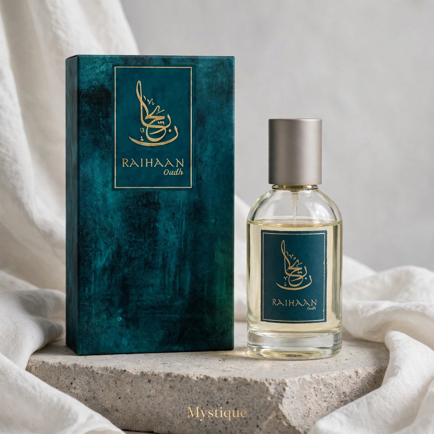 A clear glass perfume bottle with a silver cap stands beside its textured teal-green box with gold lettering reading 'RAIHAAN oudh'. The set is styled on a stone slab with draped white fabric in the background.
